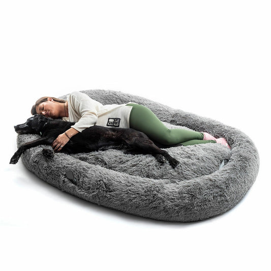 Femme allongée avec un grand chien noir sur un panier XXL ultra moelleux en fausse fourrure grise, lit géant anti-stress idéal pour offrir confort et sécurité aux grands chiens.