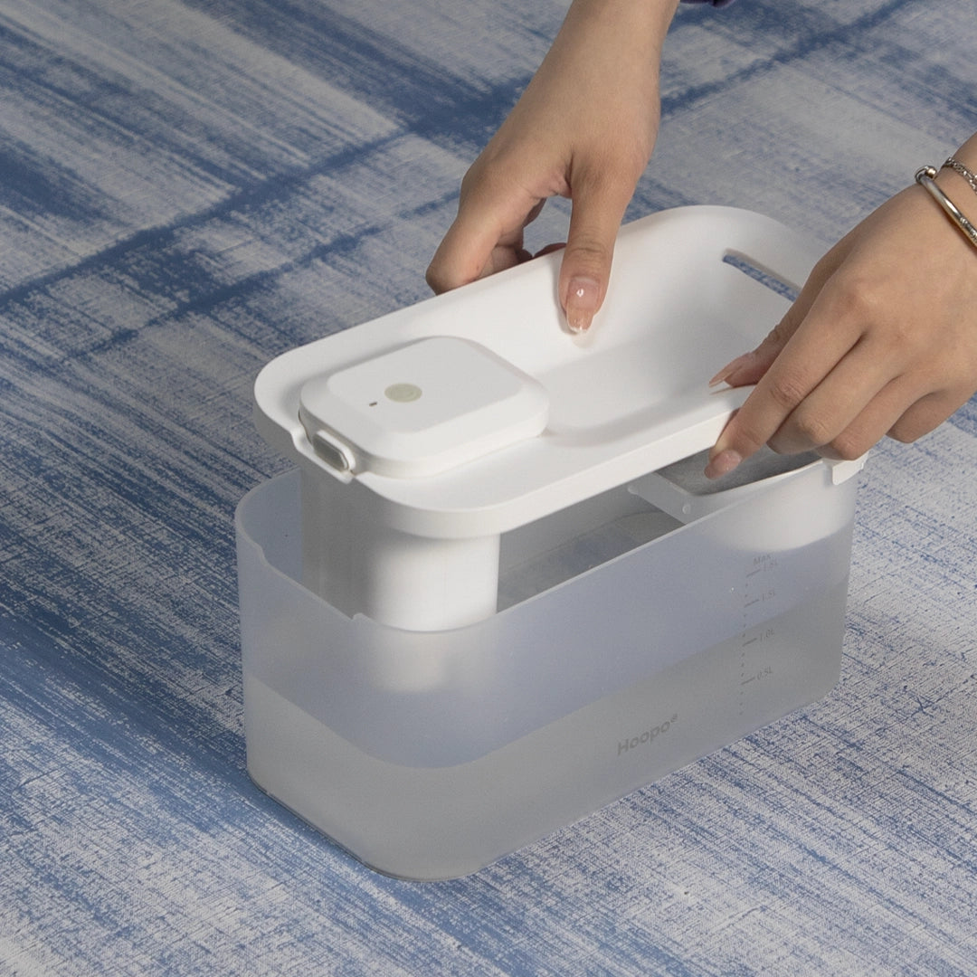 Une personne ouvre le couvercle d'un distributeur d'eau automatique Hoopo blanc et moderne, montrant sa facilité d'accès et de manipulation.