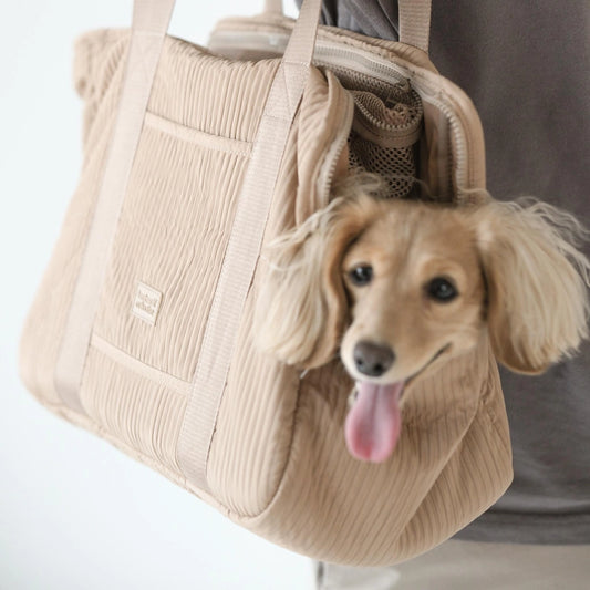Un sac de transport pour animaux beige, doté d'une fenêtre en maille, accueille un chien de petite taille. Le sac est conçu pour offrir un transport sûr et confortable.