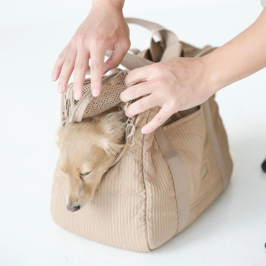 Un sac de transport pour animaux beige, doté d'une fenêtre en maille, accueille un chien de petite taille. Les mains d'une personne montrent comment manipuler la fermeture, garantissant une utilisation facile et sécurisée.