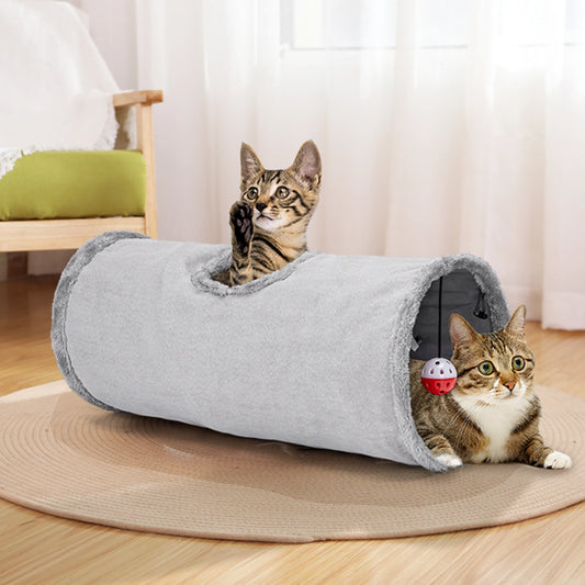 Tunnel pour chat en tissu gris doux, doté d'une boule rouge suspendue à l'intérieur. Deux chats jouent dedans, montrant son utilisation comme espace de jeu et de repos.