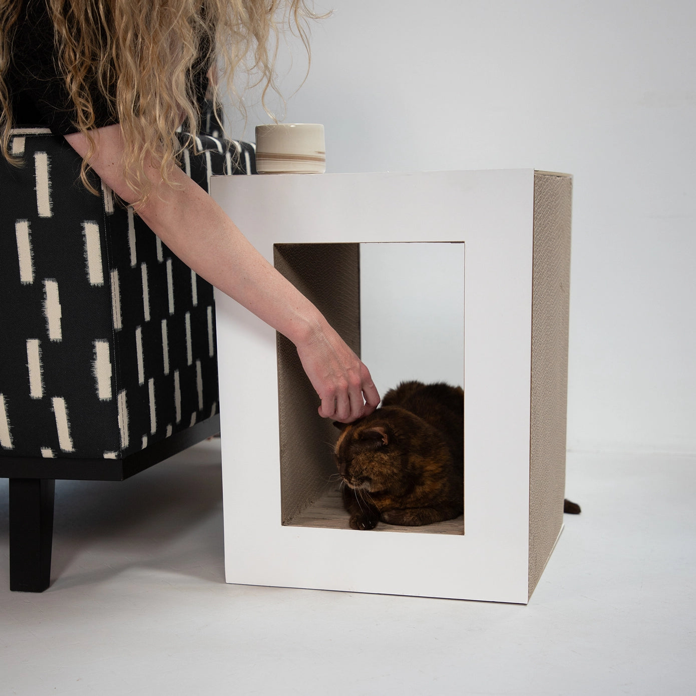 femme caressant un chat à l’intérieur de la table griffoire Hoopo en carton renforcé, montrant l’accès facile et le confort de l'abri pour félin 